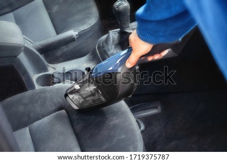 Cleaning in the car. Vacuuming front car seats with a small vacuum cleaner. Tiny hand vacuum cleaner in the hands of a Caucasian man. Home environment. Car maintenance. Cleaning in the car.  Royalty-Free Stock Photo #1719375787