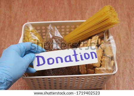 A hand in a rubber glove holds the inscription Donation. A donation box with a food . Buckwheat, spaghetti and cookies in a box. Social assistance with food.