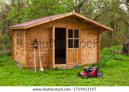 Garden shed with hoe, string trimmer,  rake and grass-cutter. Gardening tools shed. Garden house on lawn in garden. Wooden tool-shed. Hovel made of timber in domestic environment.  Royalty-Free Stock Photo #1719413197
