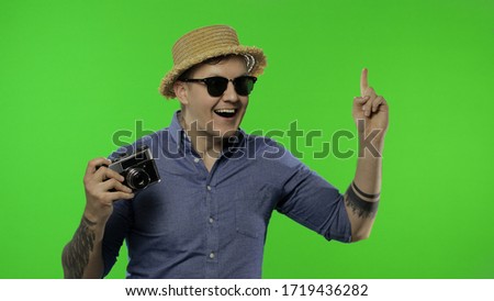 Portrait of man fashion tourist photographer getting a great idea. Handsome excited man with retro camera on vacation in blue shirt, hat and sunglasses. Place for your logo. Chroma key. Green screen
