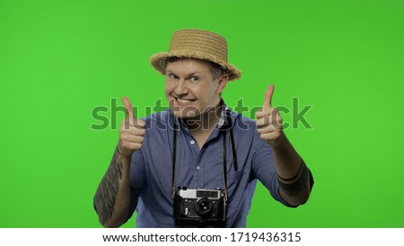 Portrait of man fashion tourist photographer giving thumbs up. Handsome man on vacation in blue shirt and hat with retro camera. Place for your logo or text. Chroma key. Green screen