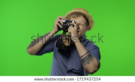 Portrait of man fashion tourist photographer is taking photos on camera. Handsome man on vacation in blue shirt and hat with retro camera. Place for your logo or text. Chroma key. Green screen