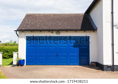 Exterior of a double garage with a blue metal up and over door attached to a house. Hertfordshire. UK. Royalty-Free Stock Photo #1719438211