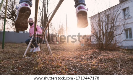 The photo is out of focus, the focus is on the sun. Sunny day, two sisters swinging on a swing near the house, the older sister in a black mask.