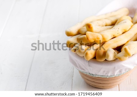 Traditional Italian bread sticks with poppy in a basket on a white wooden background.