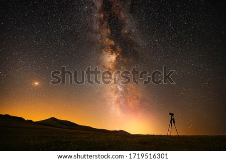 Beautfiul night landscape, silhouette of a camera on the tripod at the starry night and bright milky way galaxy.

