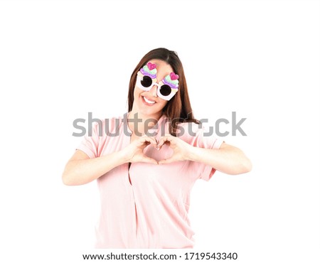 Happy young woman smiling and doing a heart gesture with both hands while wearing cupcake sunglasses against a white background