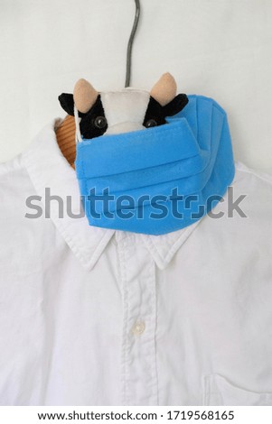 Baby toy in face mask on white shirt background. Shirt on a wooden hanger. Copy space.