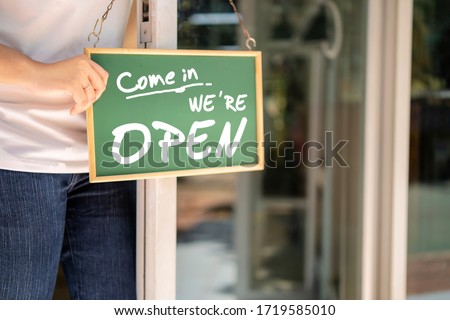 "Come in WE'RE Open" on cafe or restaurant hang on door at entrance. Asian restaurant owners are hanging a blackboard with the word welcome open to open the shop.