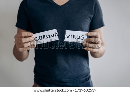 End of a coronavirus quarantine concept. Young man in blue t-shirt tears the paper with the word Coronavirus. Pandemic of COVID-19 is over. Finish of isolaion. Close up shot.