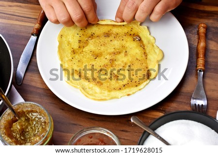 Photo from above with the close-up on a table and the hands - A person covers typical thin German pancakes with a sweet topping - delicious, homemade pancakes as a dessert in the close-up