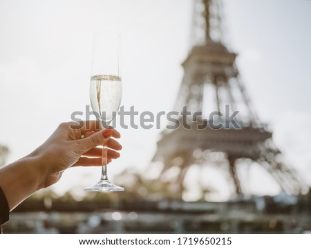 A loving couple holds in their hands glasses with expensive champagne against the background of the Eiffel Tower in Paris. The Eiffel Tower is reflected in champagne glasses. Romantic trip to Paris