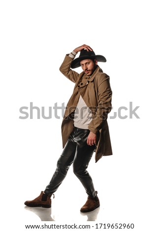 Attractive young stylish man posing in beige long coat and black hat