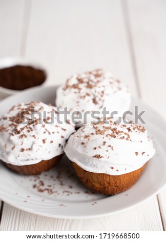Cupcakes with whipped cream and chocolate chips on a white plate and a Cup of coffee in the background, on a white wooden table. Image for the menu or catalog of confectionery products.
