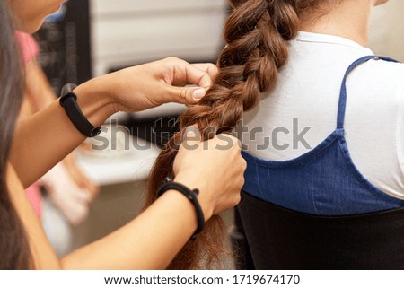 Hairstylist makes a braid to a female client in a beauty studio