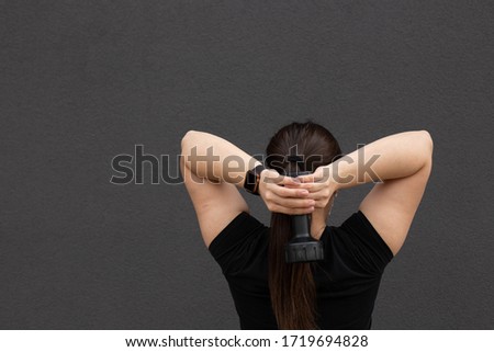 Athletic woman slim figure dumbbells behind her dark clothing.
