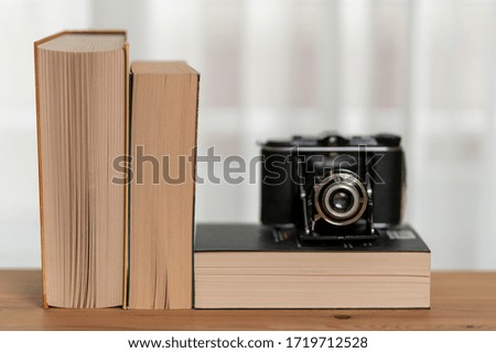 There are three books on the shelf in front of the window curtain. An old analog camera