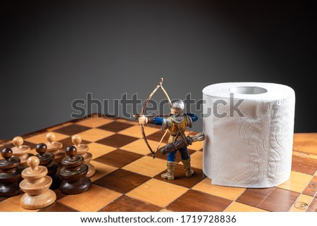 Archer defending a roll of toilet paper from an army of pawns on a chessboard. Conceptual image representing egoism and avarice during coronavirus or 2019-ncov crisis Royalty-Free Stock Photo #1719728836