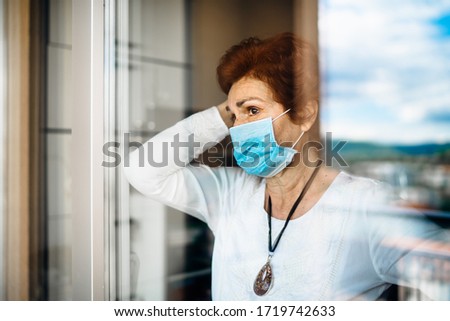 Senior elderly sad woman at home looking through the window.Coronavirus COVID-19 disease outbreak infection risk.Lockdown socialization restriction activity.Quarantine mental health effect Royalty-Free Stock Photo #1719742633