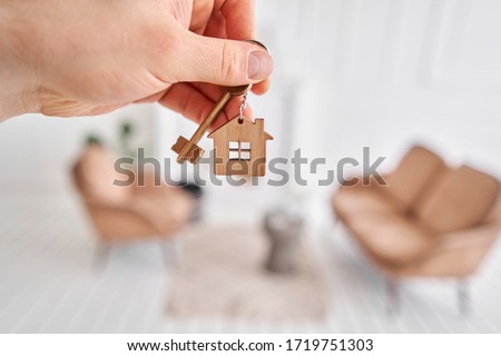 Men hand holding key with house shaped keychain. Modern light lobby interior. Mortgage concept. Real estate, moving home or renting property. Royalty-Free Stock Photo #1719751303