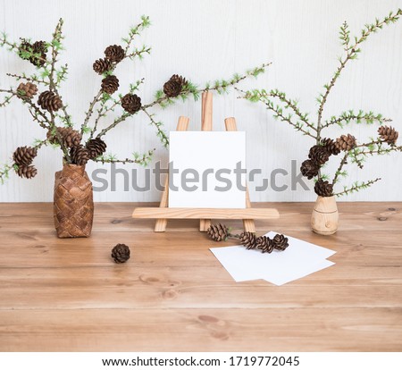 Interior Design Desktop with Mock up Poster Frame. Blank Paper Card Mockup on a Mini Easel and Larch Branches with Cones. Stylish Minimal Home Decor