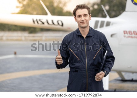 Picture of helicopter mechanic standing by a chopper. He is inspecting the helicopter for final safety check before taking off. He is holder a black folder which held safety check list paper.
