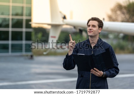Picture of helicopter mechanic standing by a chopper. He is inspecting the helicopter for final safety check before taking off. He is holder a black folder which held safety check list paper.