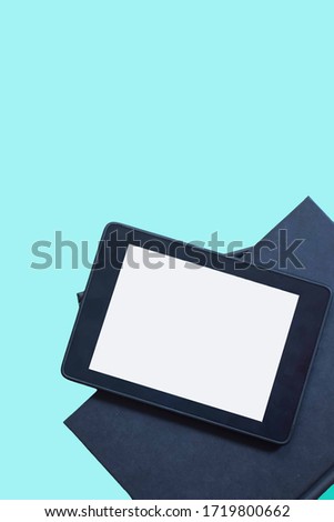 Tabletop view, mockup the blank screen of a tablet on top of a stacked notebook blue background