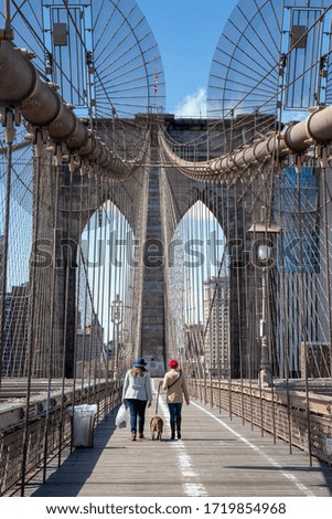 View of two ladies walking a dog on an empty Brooklyn Bridge with the Manhattan Skyline in the background during the Coronavirus pandemic in New York City