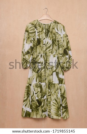Women's sundress dress with a banana, palm,bamboo leaves pattern Isolate on hanging –wooden background
