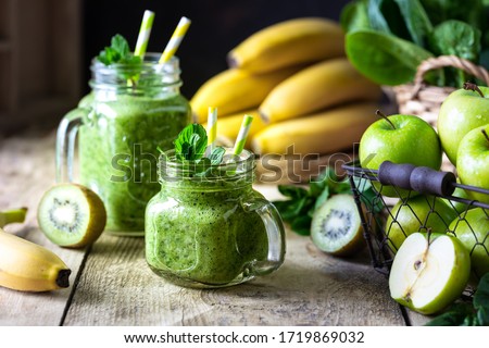 Two healthy green smoothies with spinach, banana, apple, kiwi and mint in glass jar and ingredients. Detox, diet, healthy, vegetarian food concept Royalty-Free Stock Photo #1719869032