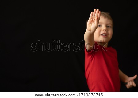 Cheerful boy in a red t-shirt shows on his fingers that he is four years old, smiling and standing over black background. Image with selective focus and toning. Space for your text