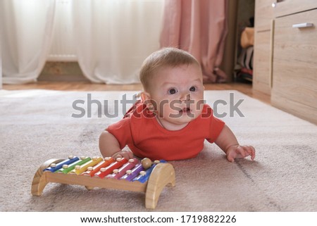 little happy baby, child in a red suit lies on the carpet playing with colorful toy xylophone