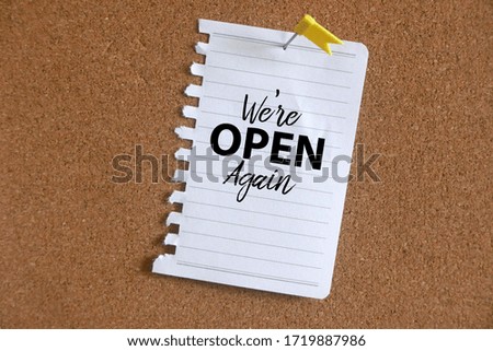 Paper on a cork board written with ' We're Open Again '.