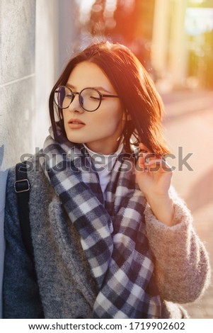 Attractive young girl wearing glasses in a coat on a urban background walking on a sunny day