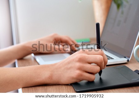 Young red-haired woman graphic designer working from home side hustle holding pen using drawing tablet and laptop close-up