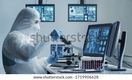 Scientist in protection suit and masks working in research lab using laboratory equipment: microscopes, test tubes. Coronavirus 2019-ncov hazard, pharmaceutical discovery, bacteriology and virology. Royalty-Free Stock Photo #1719906628