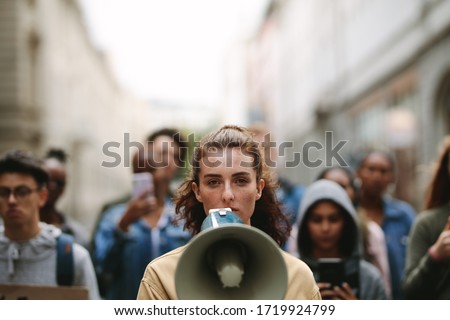 Young woman with a megaphone with group of demonstrator in background. Woman protesting with megaphone in the city. Royalty-Free Stock Photo #1719924799