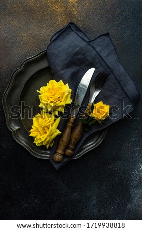 Table setting with yellow roses and cutlery on rustic table with copy space