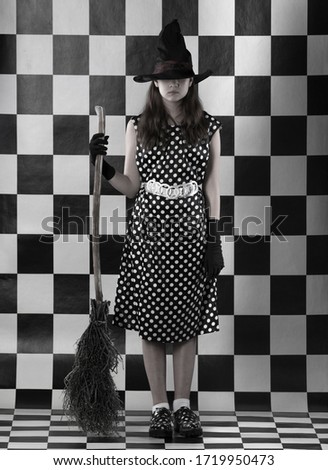 young woman witch in a polka-dot dress and with a broom on chess background