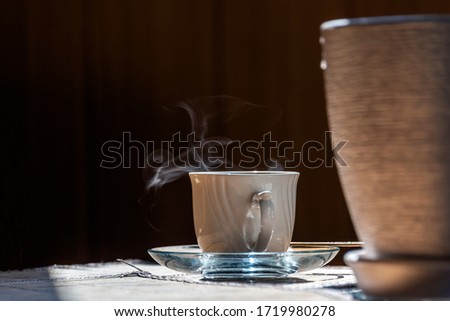 A cup of hot coffee on a table near a flower pot.