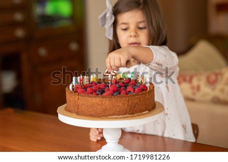 Little girl at home looks at a birthday cake. On the cake there is a candle for 4 years and an inscription of letters-candles in Russian "Happy Birthday". Image with selective focus.