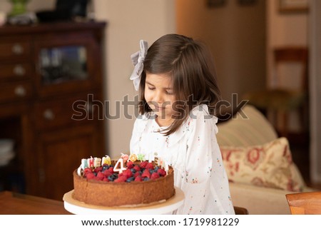Little girl at home looks at a birthday cake. On the cake there is a candle for 4 years and an inscription of letters-candles in Russian "Happy Birthday". Image with selective focus.