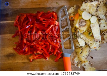 Artisanal preparation of a homemade mixed vegetable dish in a kitchen : fresh red peppers cut into slices, peelings of pineapple and a knife with hollow ground blade on a wooden chopping board Royalty-Free Stock Photo #1719983749