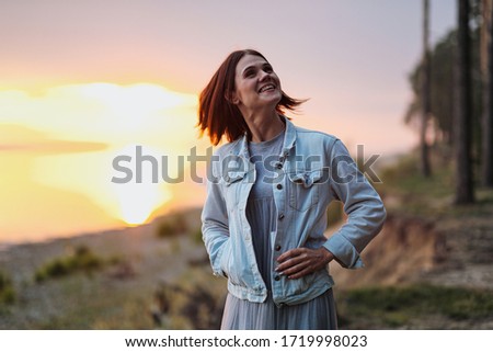 Attractive young red-haired woman with a short haircut at sunset in the woods. Rest in nature.