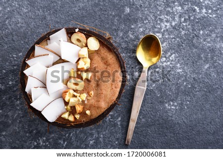top view chocolate smoothie with coconut, nuts in coconut bowl, smoothie bowl concept, dessert spoon on gray background, copy space