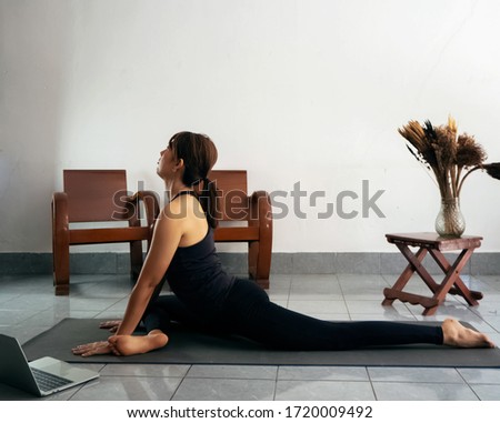 Woman wearing exercise suit ,strteching body on yoga mat,learning form laptop,at home