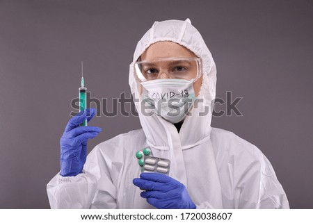 Young woman in protective costume, glasses and protective mask with "COVID-19" sign. Vaccine against coronavirus, flu, ebola, tuberculosis, virus. Personal protective equipment against COVID-19.