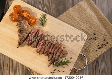 Slice Juicy grilled steak medium rare beef on wooden cutting board with tomato and rosemary , wooden table - Stock photo