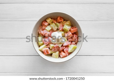 Fresh salad with tomato and cucumber, seasoned with sour cream. Placed on white wooden table. Top view